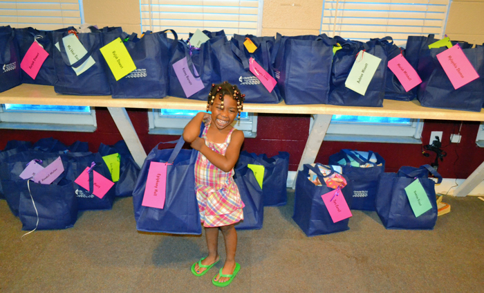 A little girl from the Homeless Family Center shows off all of the donated bags filled with school supplies, clothes and other items.